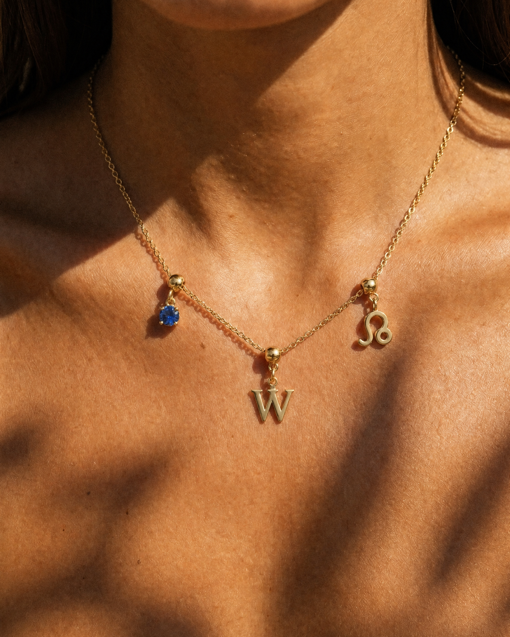 Gold initial W charm station necklace on model with Leo zodiac and sapphire