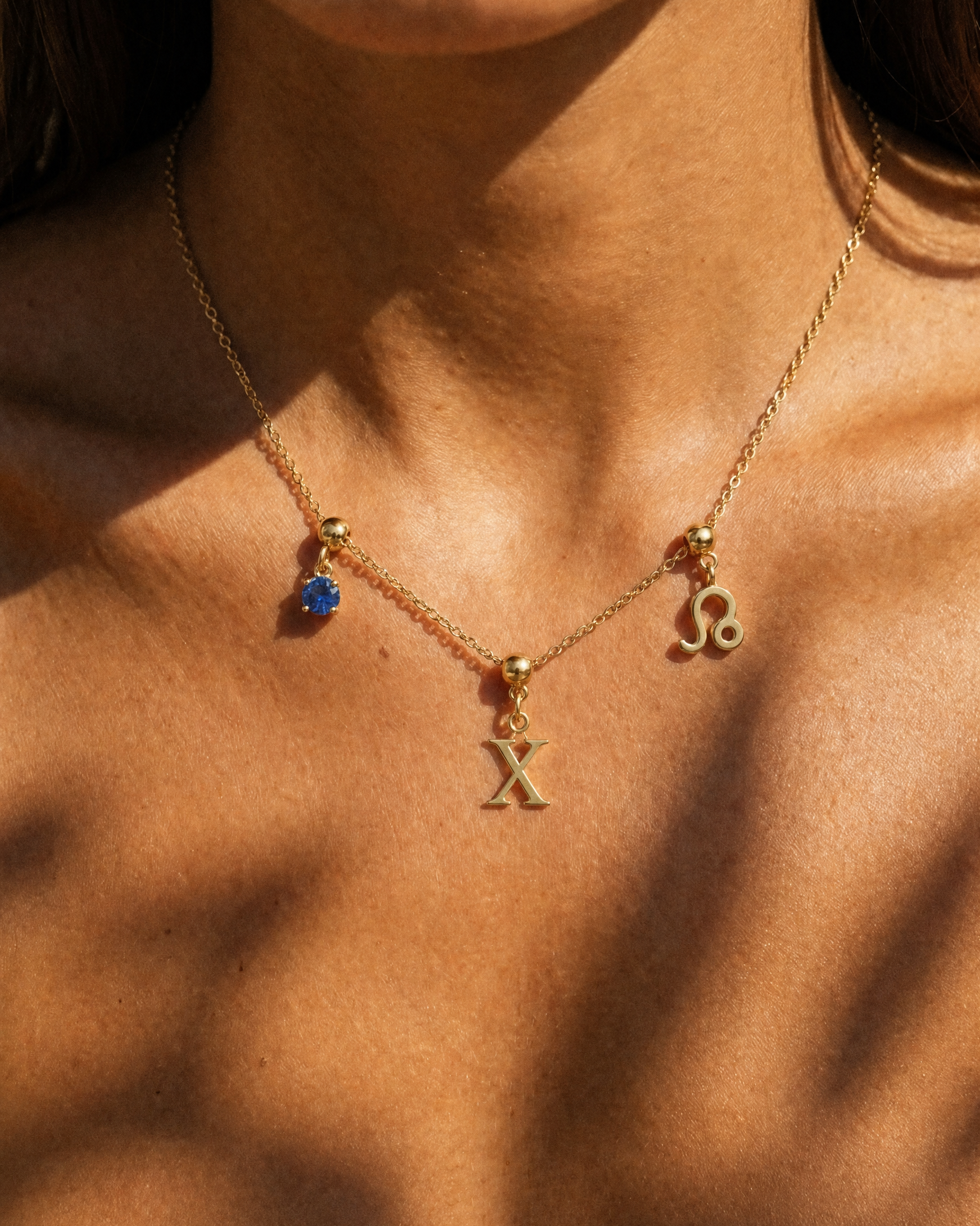 Gold initial X charm station necklace on model with Leo zodiac and sapphire