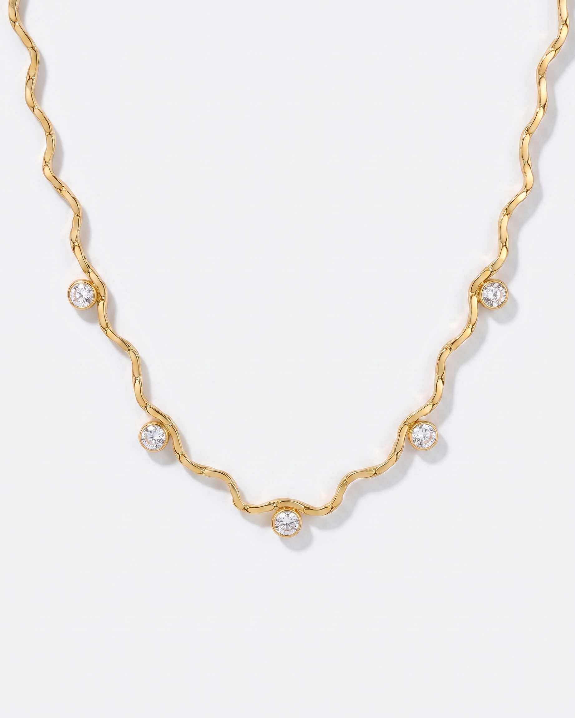 Riviere wavy gold chain necklace with zircon stations on off white background