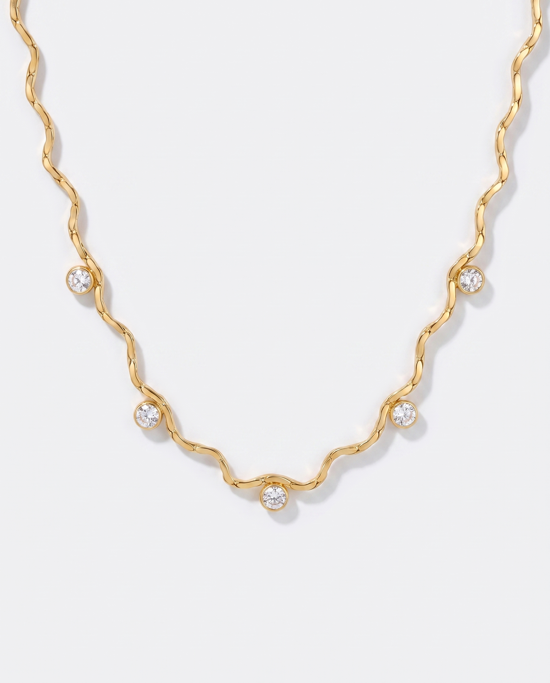 Riviere wavy gold chain necklace with zircon stations on off white background