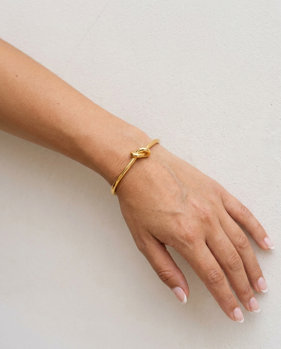 Elise Gold Knot Bangle on wrist plaster wall
