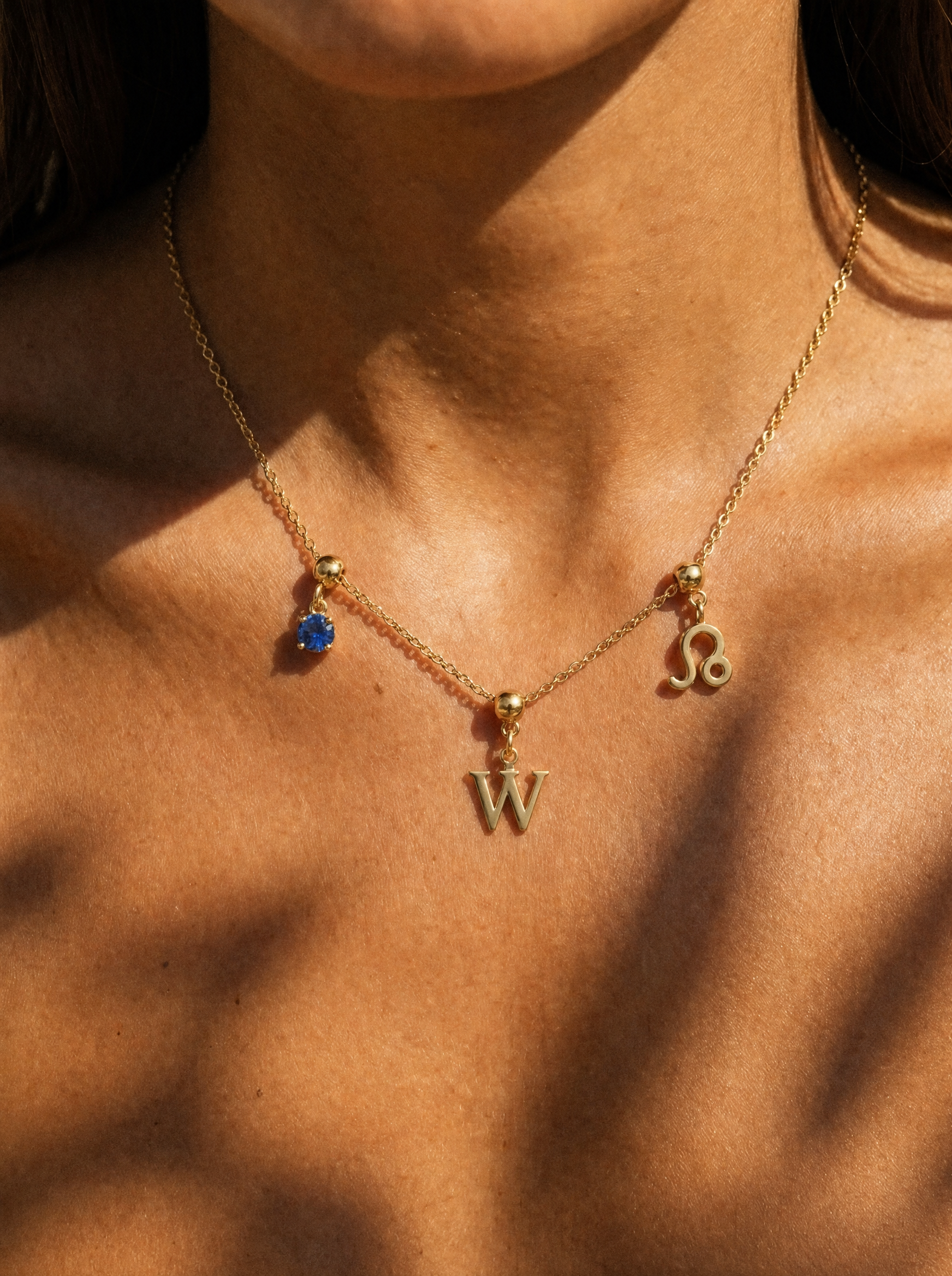 Gold initial W charm station necklace on model with Leo zodiac and sapphire