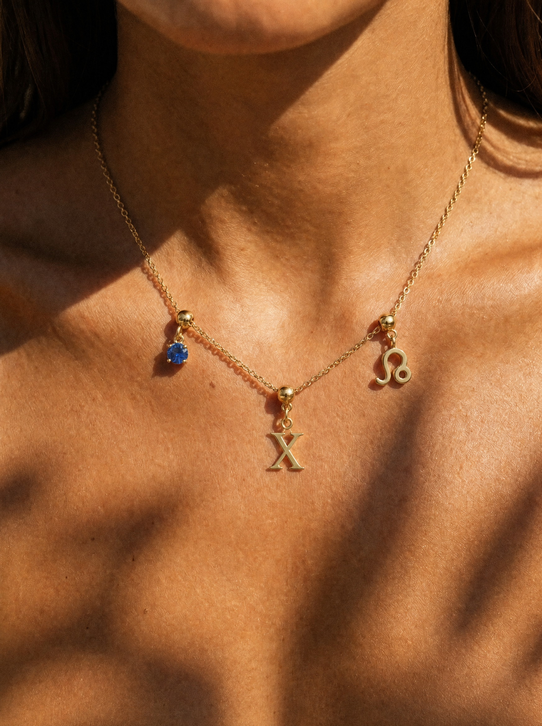 Gold initial X charm station necklace on model with Leo zodiac and sapphire
