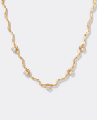 Riviere wavy gold chain necklace with zircon stations on off white background